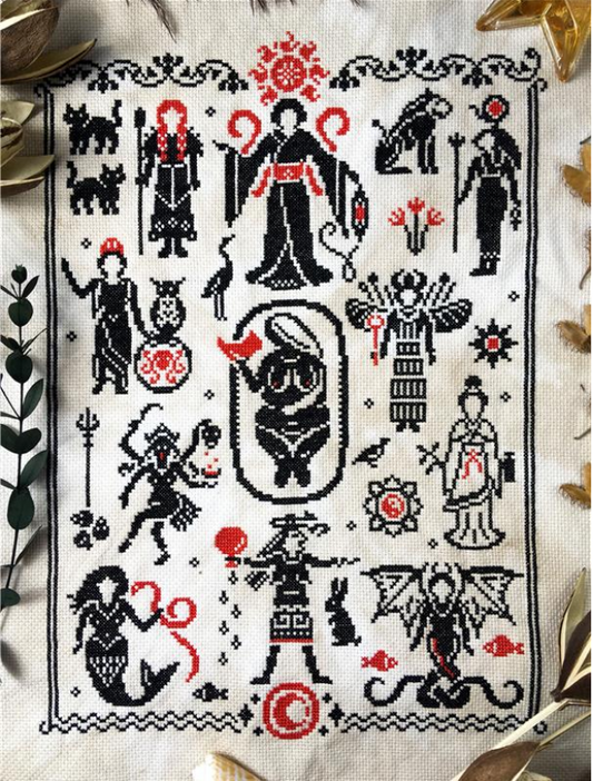 A cross stitch sampler stitched in black with red highlights, containing motifs of various Goddesses and sacred beings. The piece is surrounded by a border with waves at the bottom and vines up the top